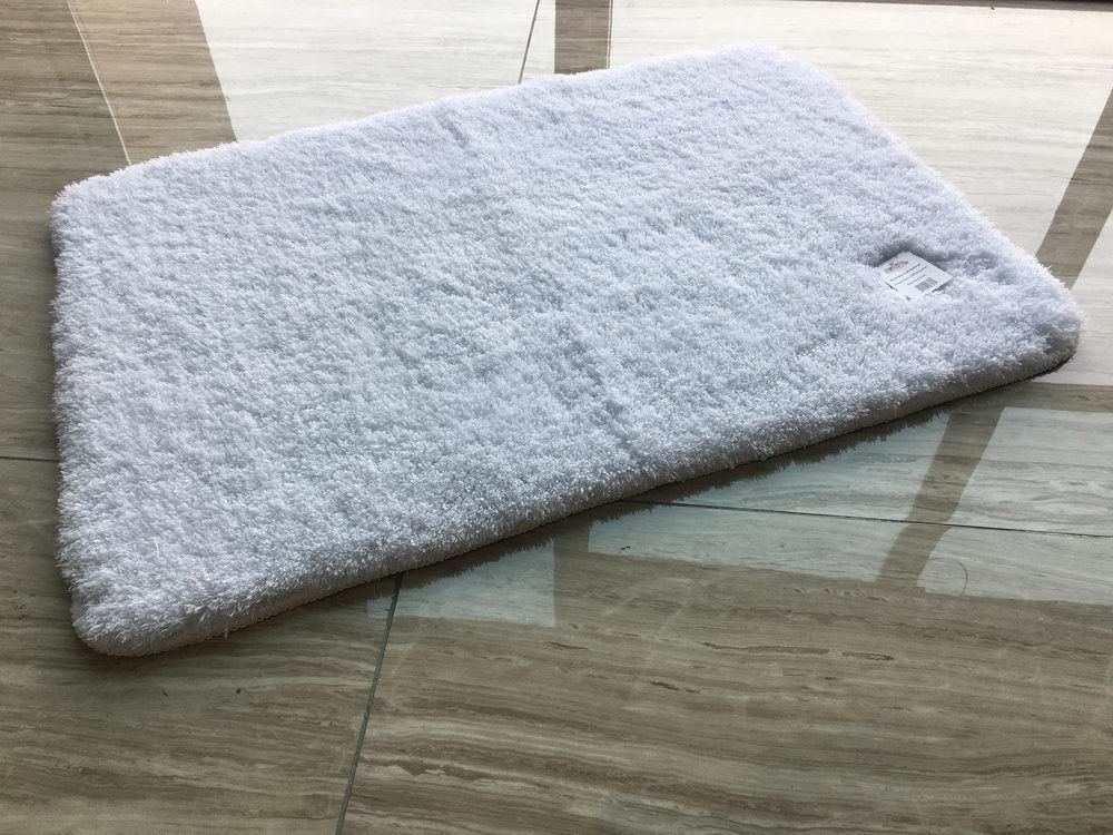 A white bath mat is sitting on a tiled floor.