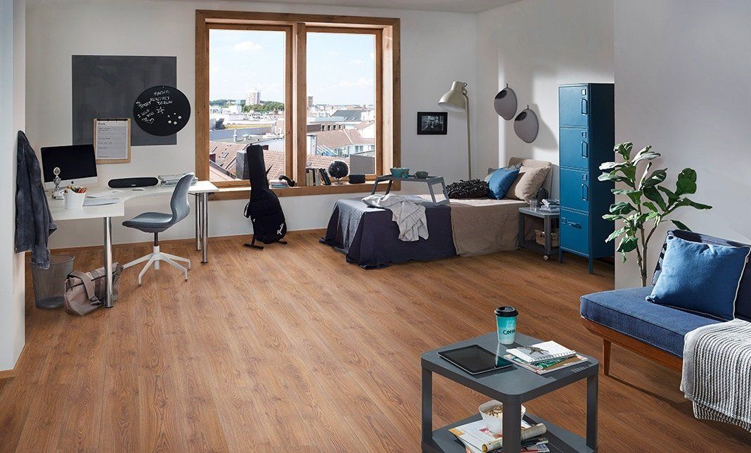 A living room with a wooden floor , a couch , a desk and a window.