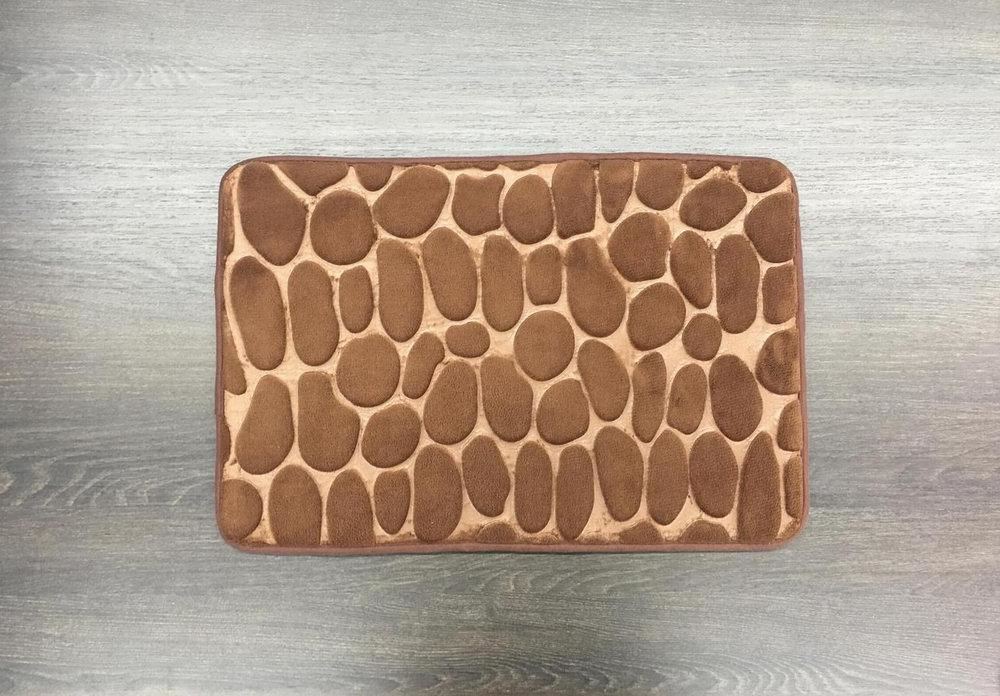 A brown rug with a pattern of rocks on it is on a wooden floor.