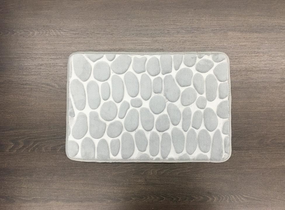 A white bath mat with a pattern of rocks on it is sitting on a wooden table.