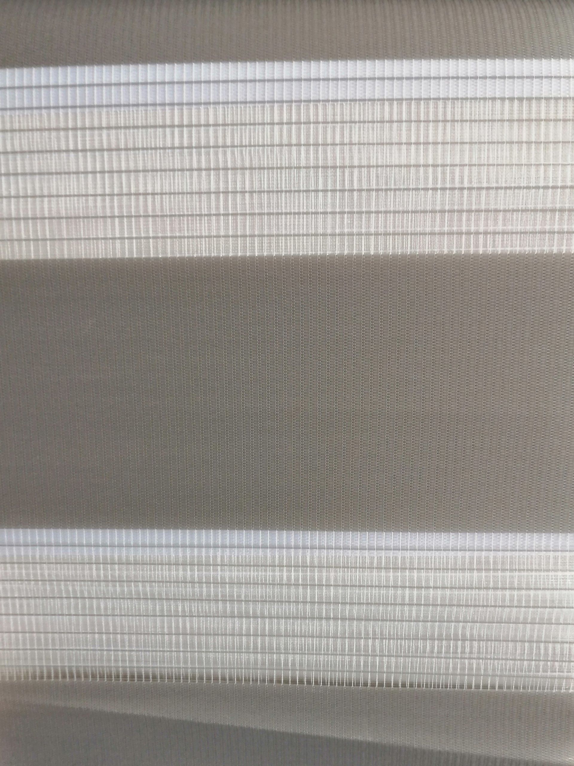 A close up of a gray and white blind on a window.
