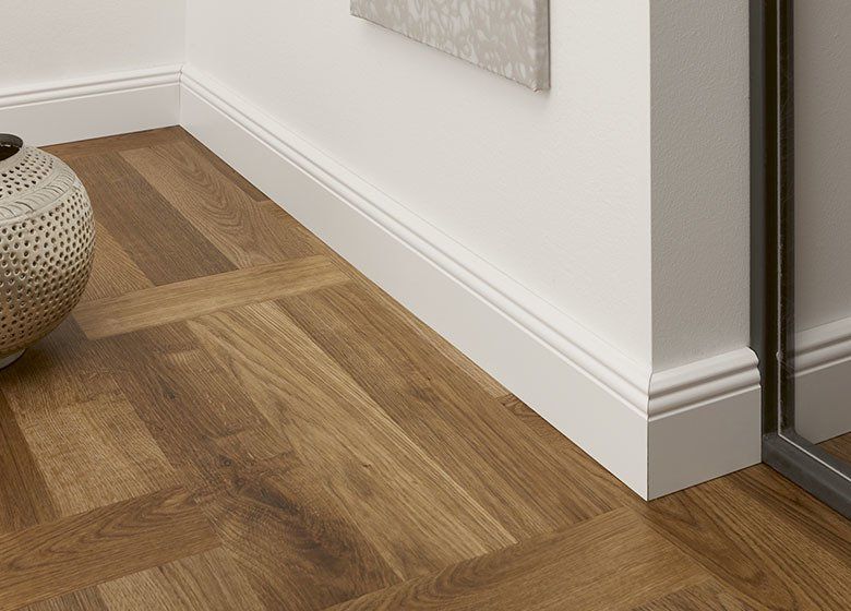 A vase is sitting on a wooden floor next to a white wall.