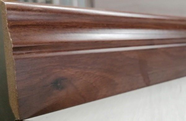 A close up of a wooden skirting board on a white surface.