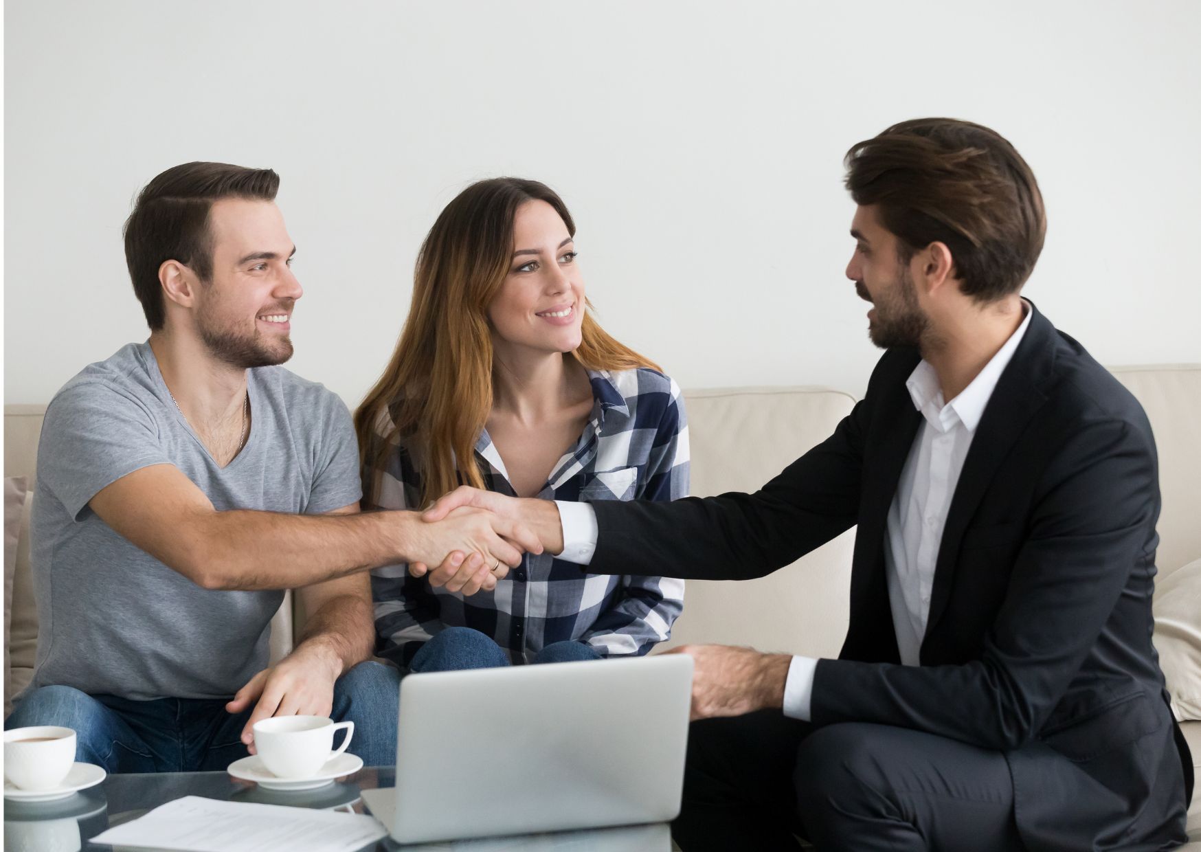 Three people on couch, handshake with suited professional, laptop and papers on table.