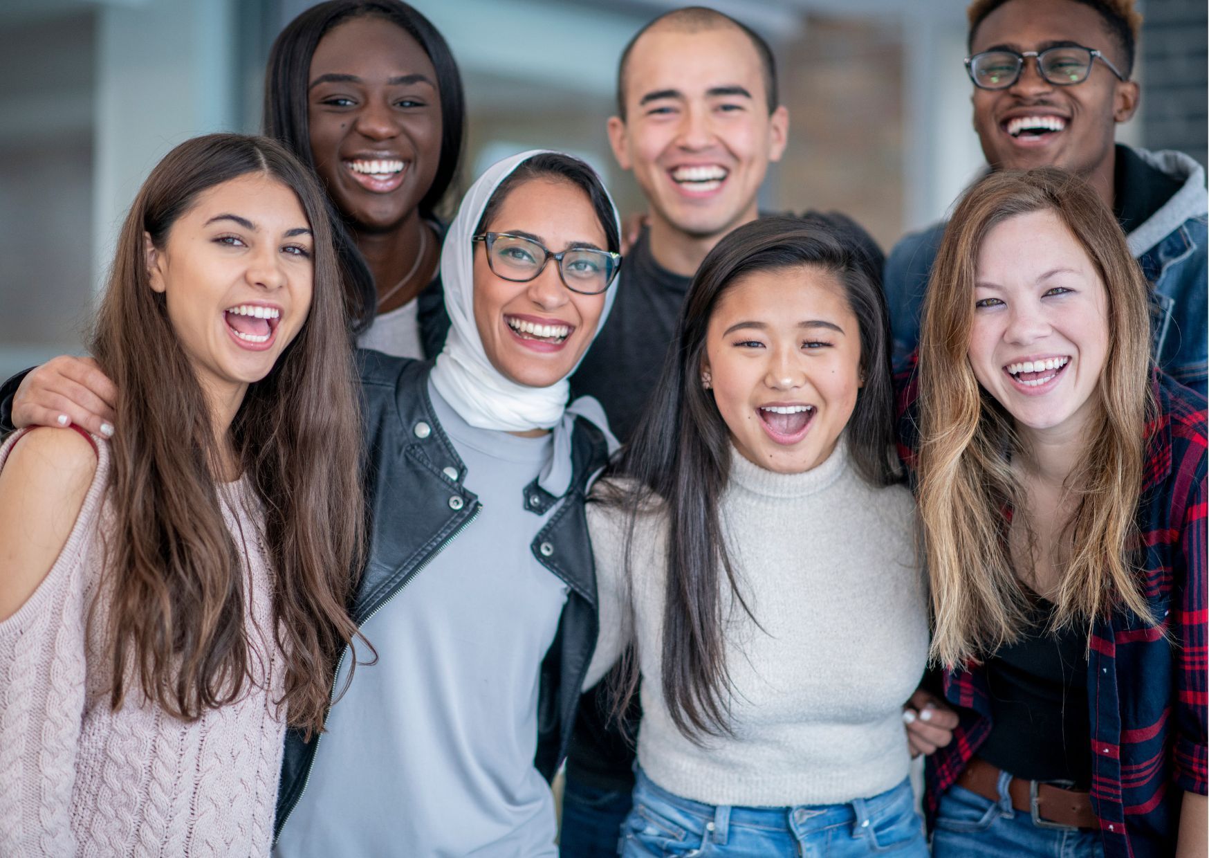 Seven young adults smiling together indoors, dressed casually, highlighting diversity, friendship, and inclusivity.