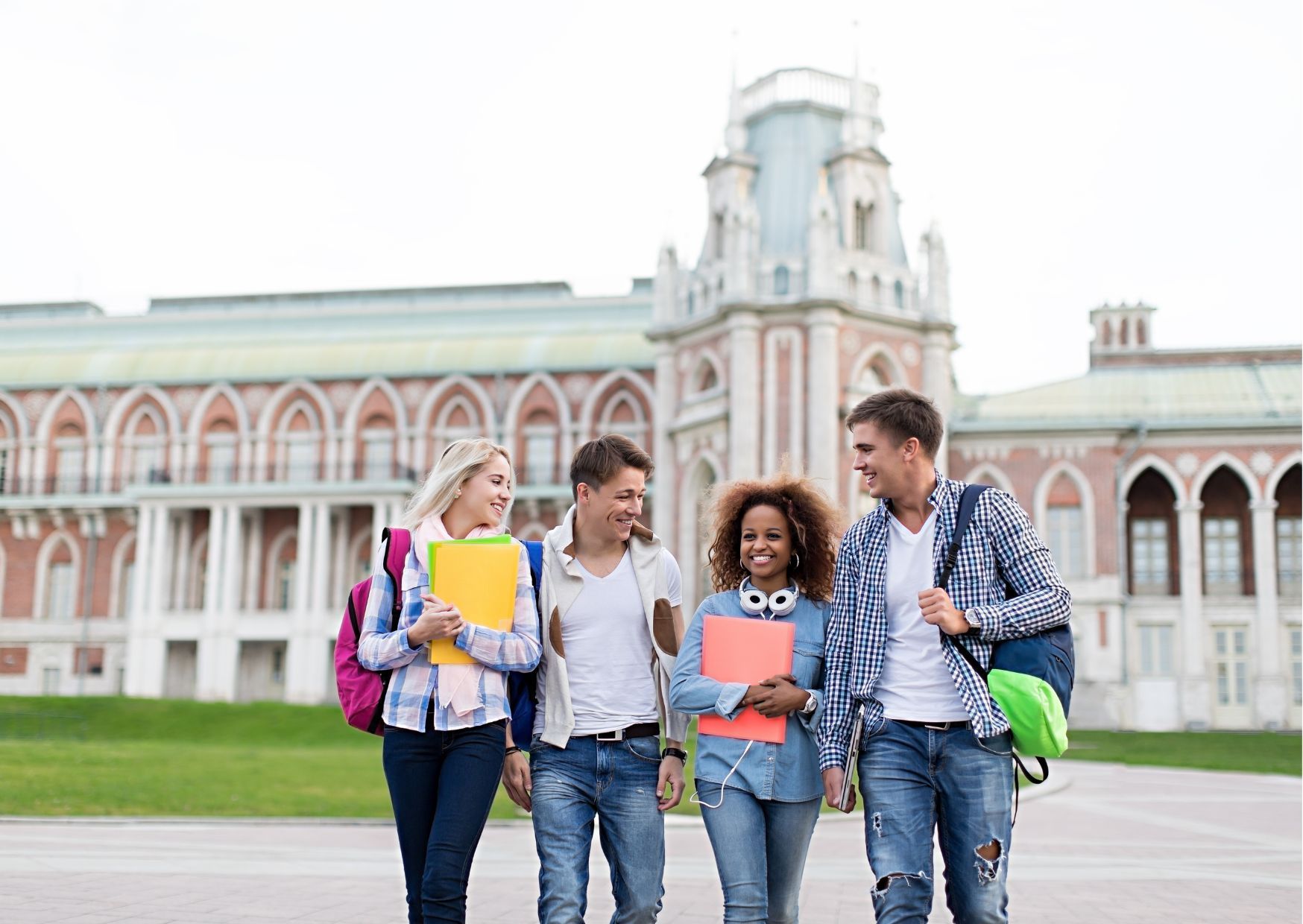 Four students with backpacks and books walking together in front of ornate university building with 