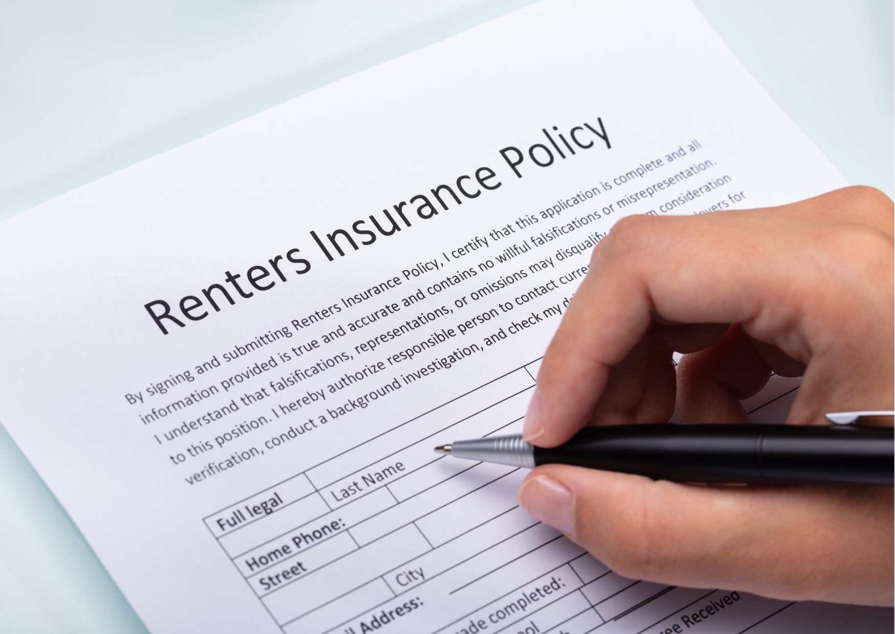 Person filling renters insurance policy form with pen, personal details section visible.