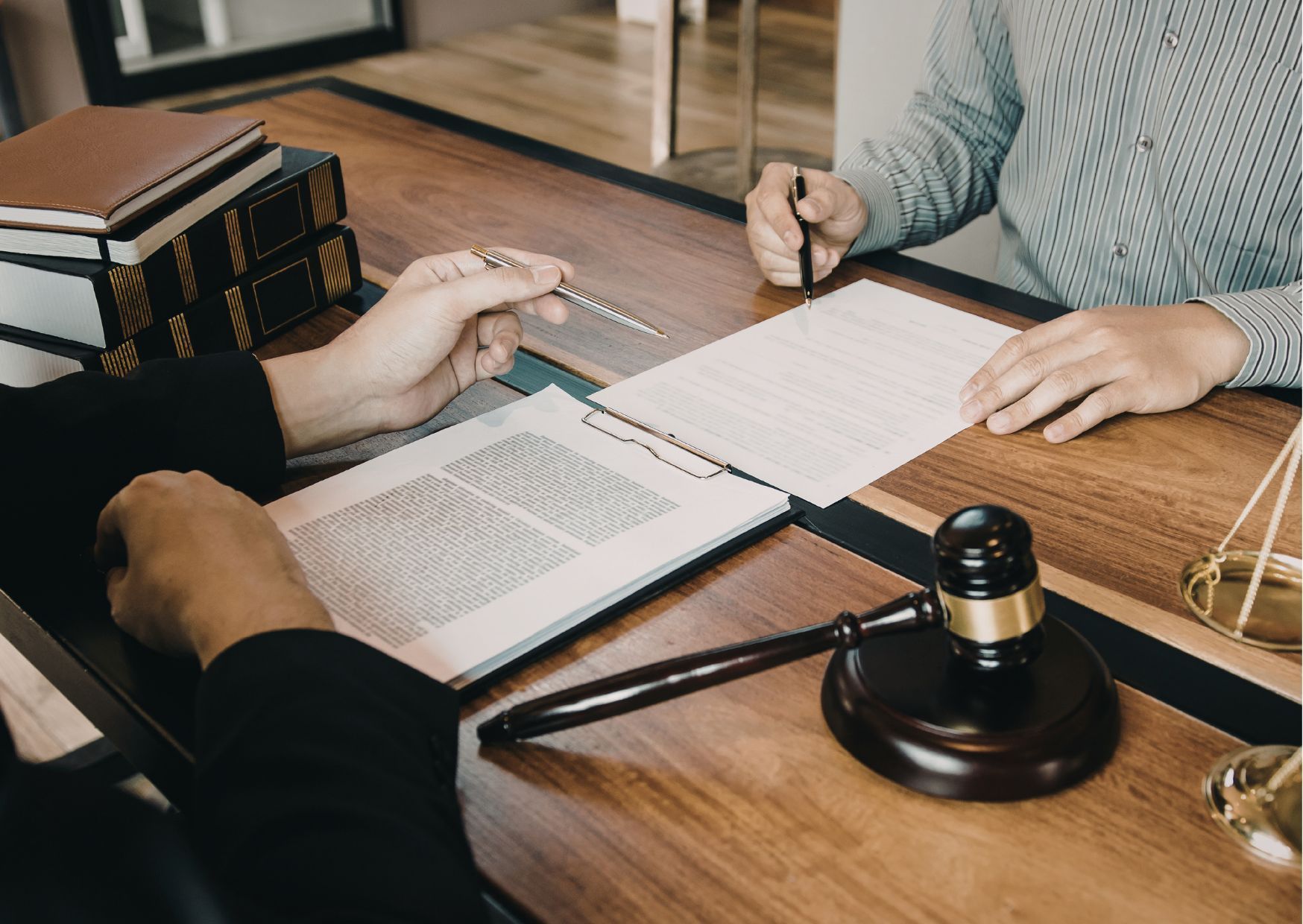 Two people reviewing documents with gavel, scales of justice, and law books on desk.