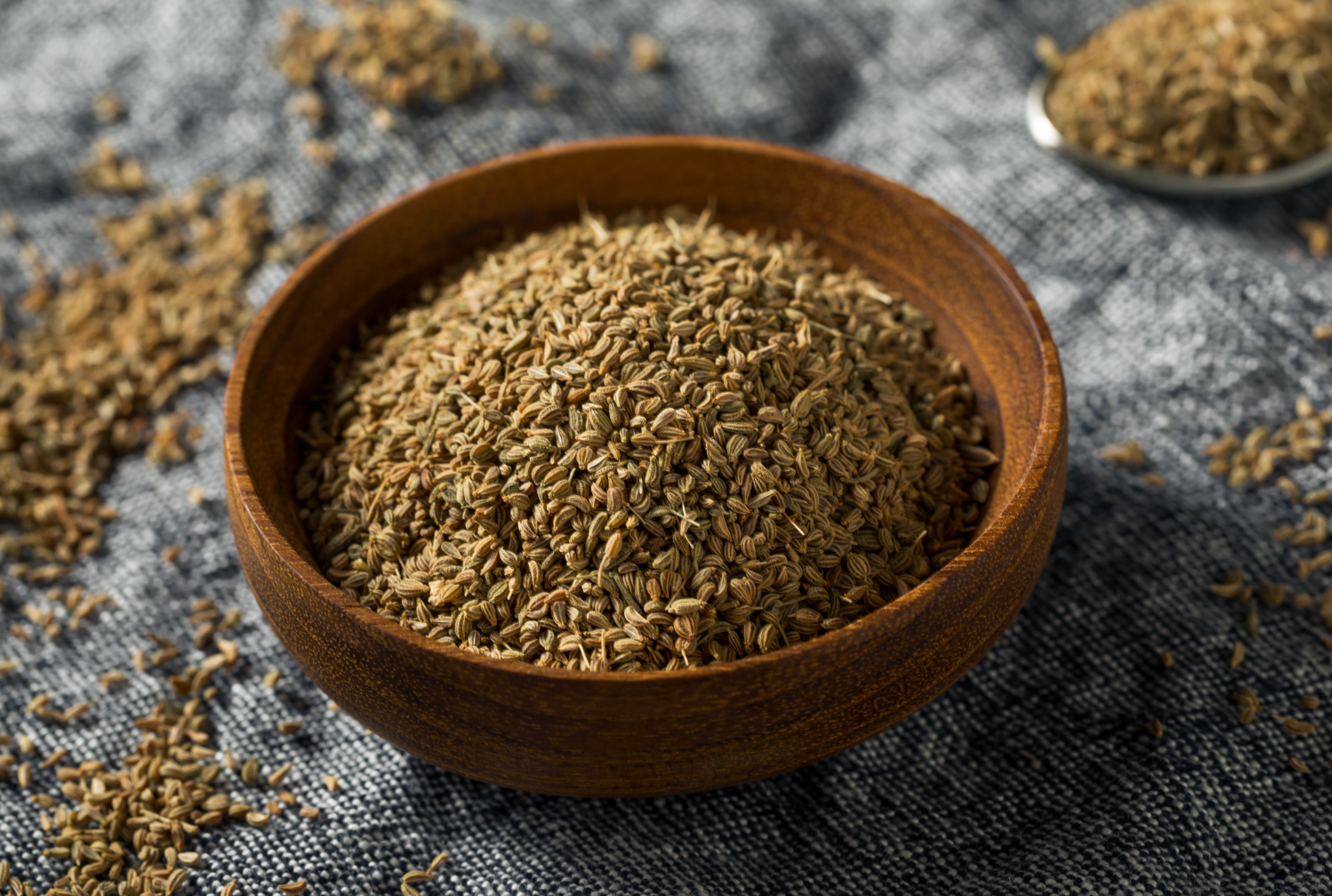 Wooden bowl filled with ground caraway seeds, on a textured blue surface.