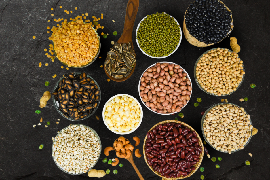 Assortment of beans and nuts in small bowls on a dark surface, including peanuts, kidney beans, and cashews.