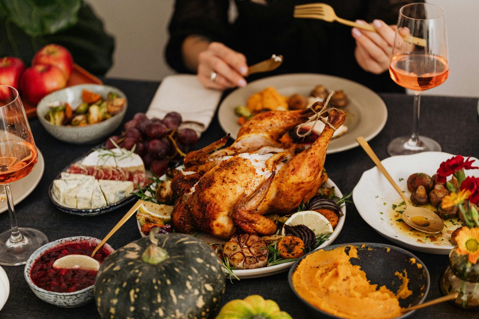 Thanksgiving dinner spread: roasted turkey, side dishes, seated person with cutlery.