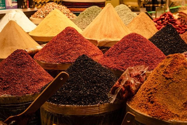 Colorful mounds of spices in a market, including red, yellow, and black, displayed in various bins.
