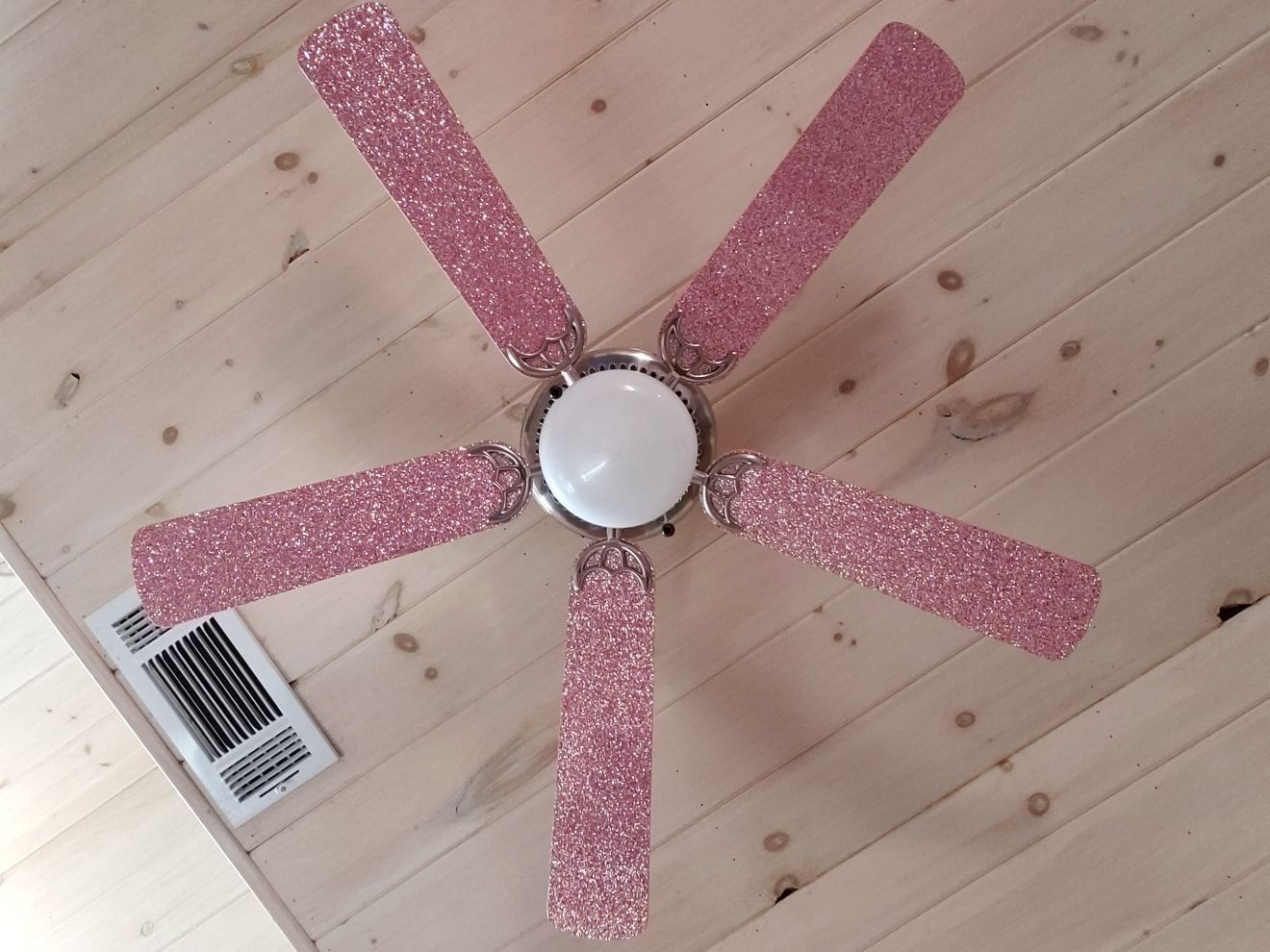 Pink glitter ceiling fan on a light wood ceiling.