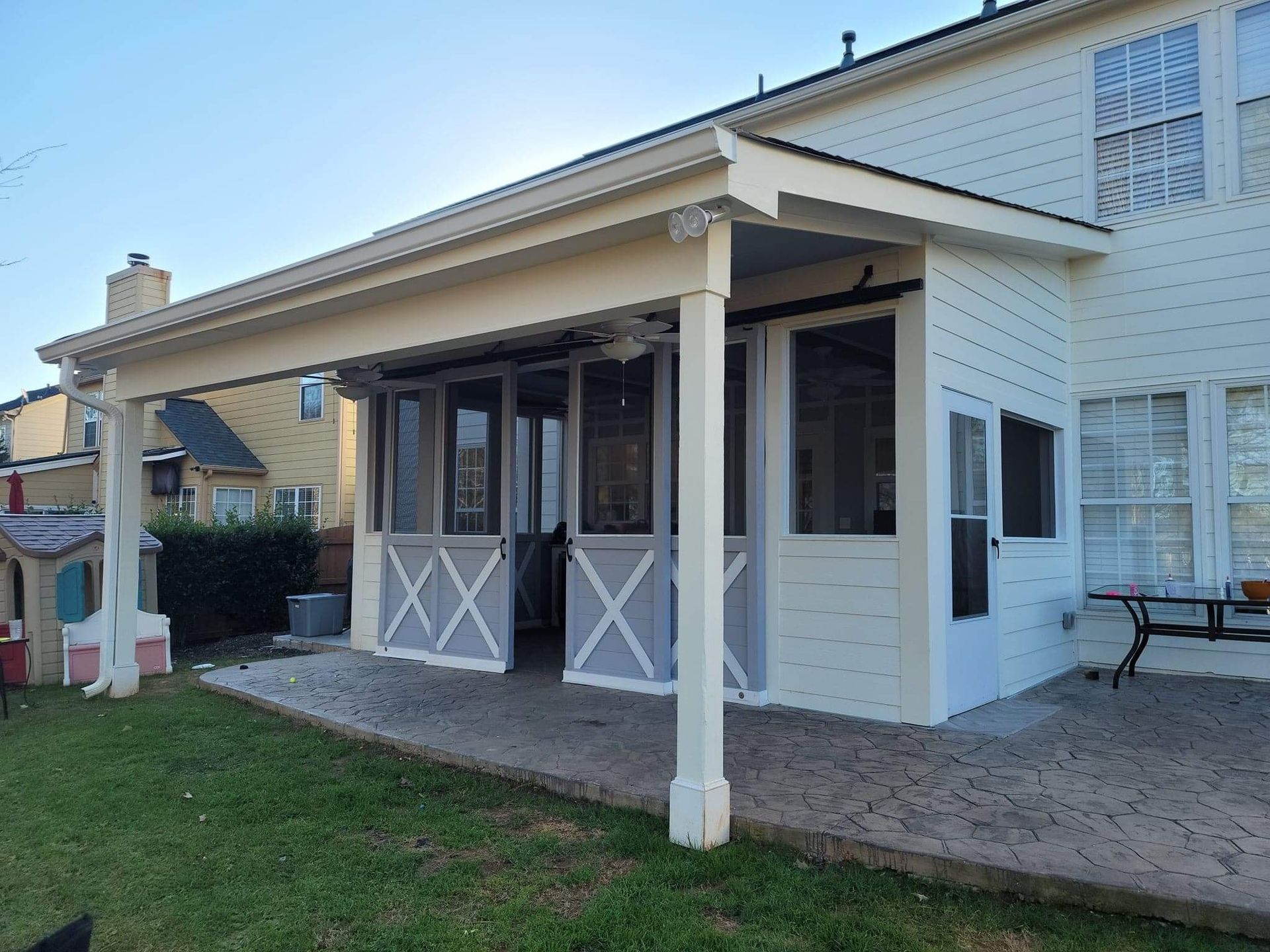 Screened-in patio with light gray barn doors, attached to a two-story white house with a green lawn.