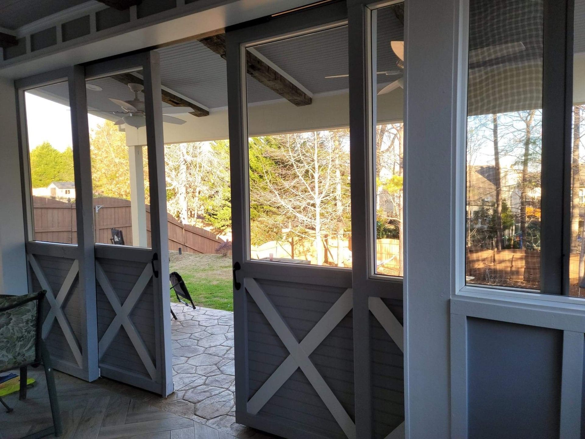 Gray barn-style sliding doors open to a sunny outdoor patio, with a view of trees and houses.