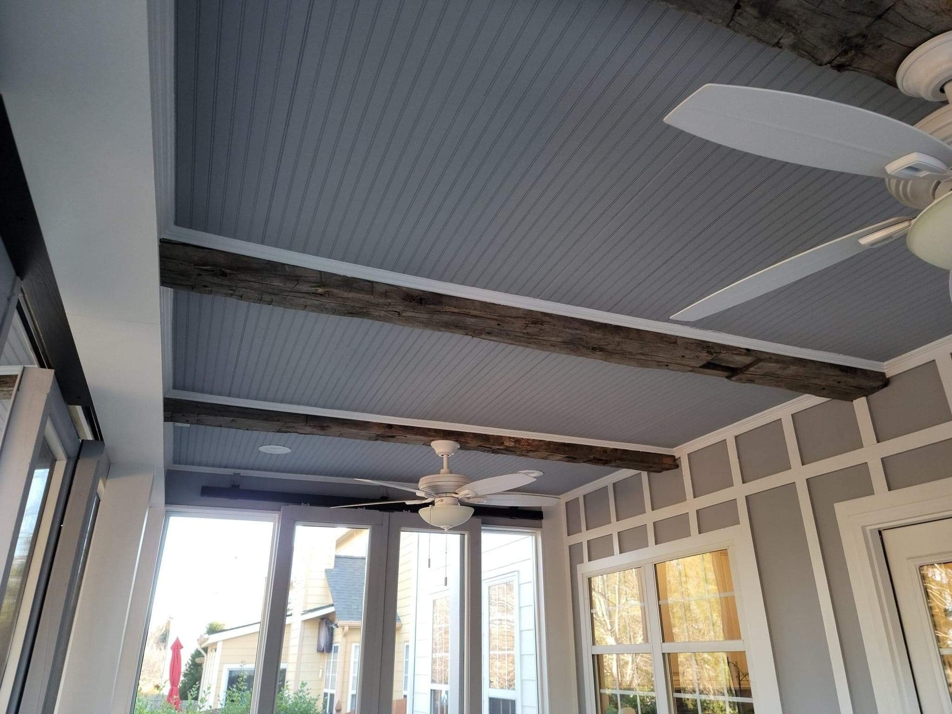 Outdoor porch ceiling with gray beadboard, weathered beams, and white trim.
