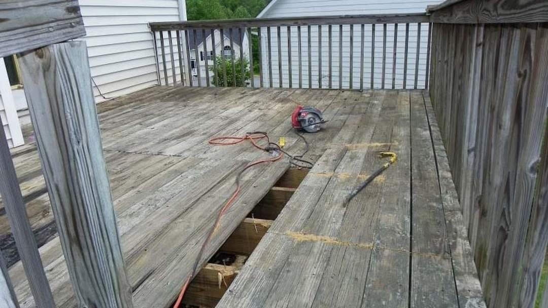 A wooden deck with a section removed, tools present. Weathered wood, exterior setting.