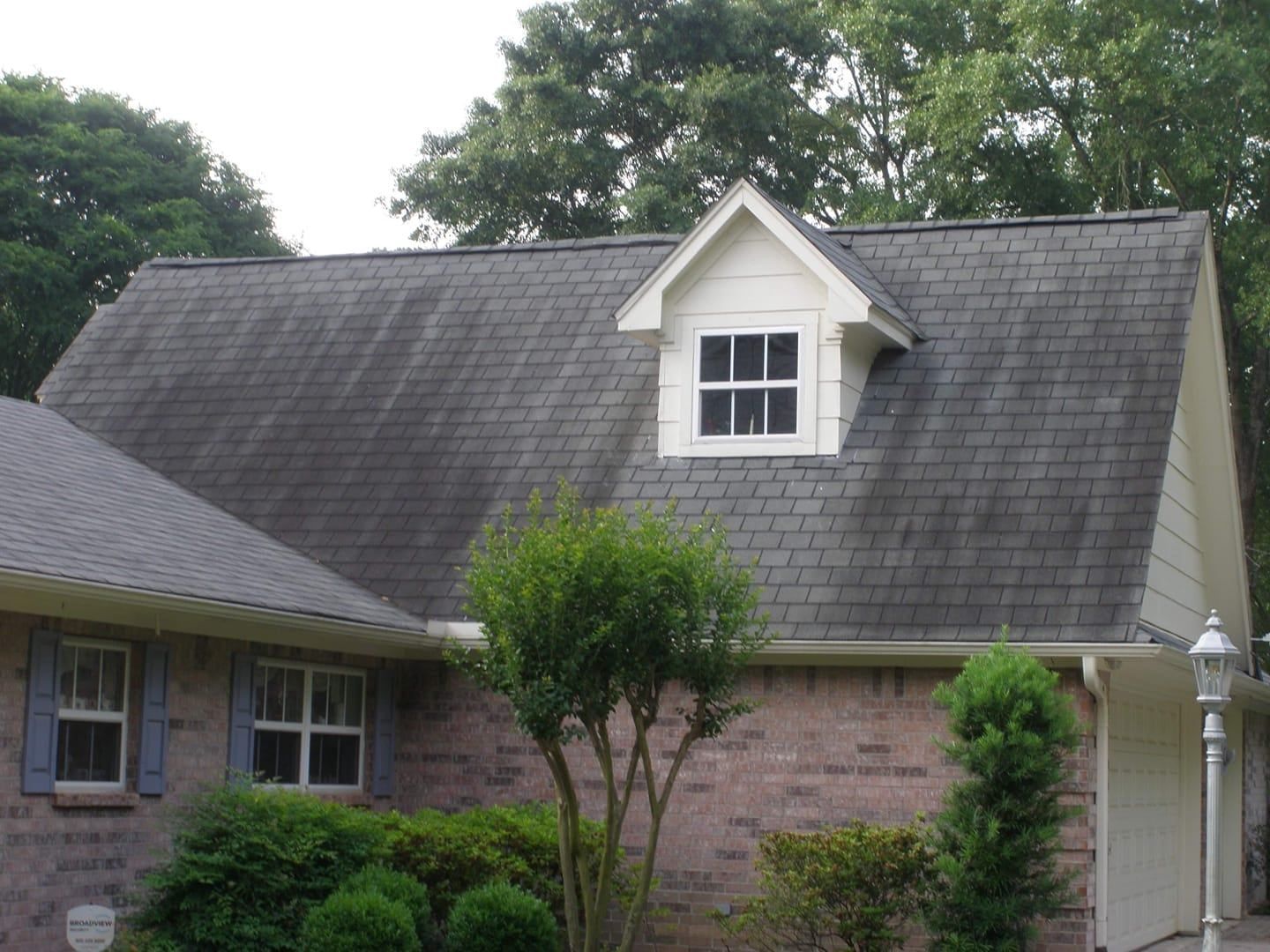 A house with a dark, mossy roof, a small dormer window, and red brick siding.