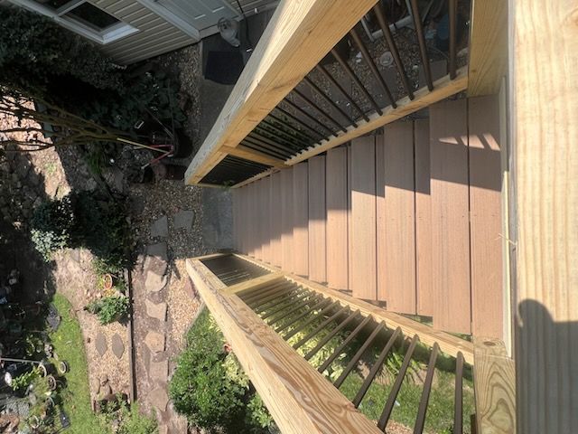 Wooden staircase with black railing, descending to a gravel path and yard.