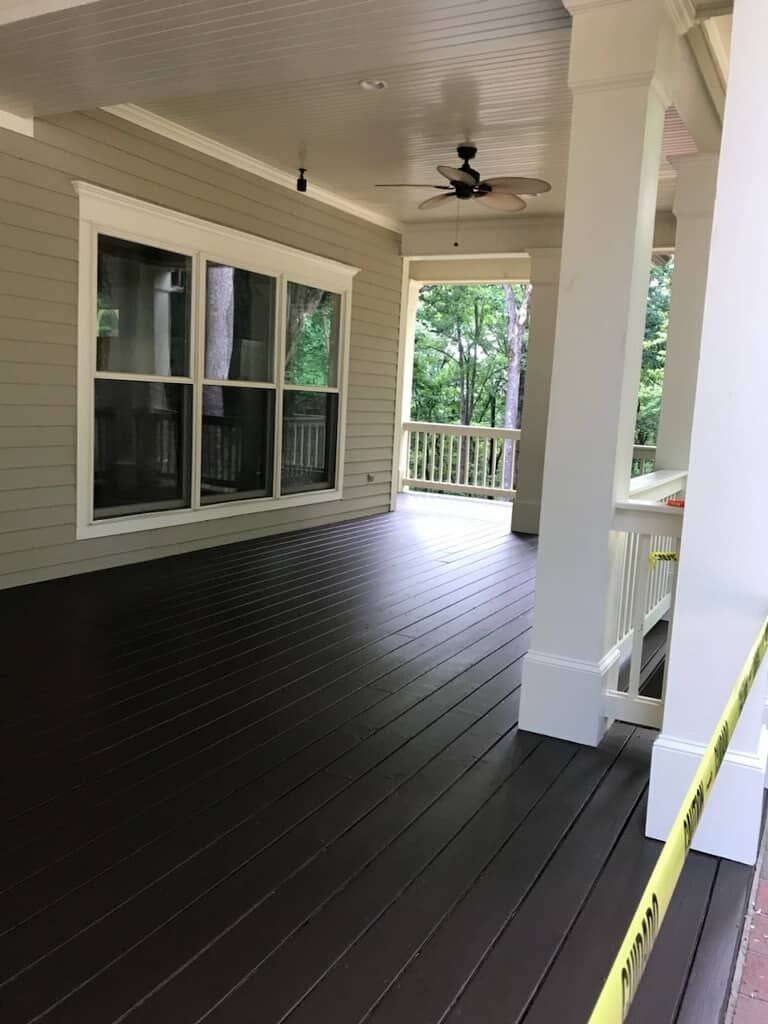 Covered porch with dark brown floor, white columns, and a view of trees.