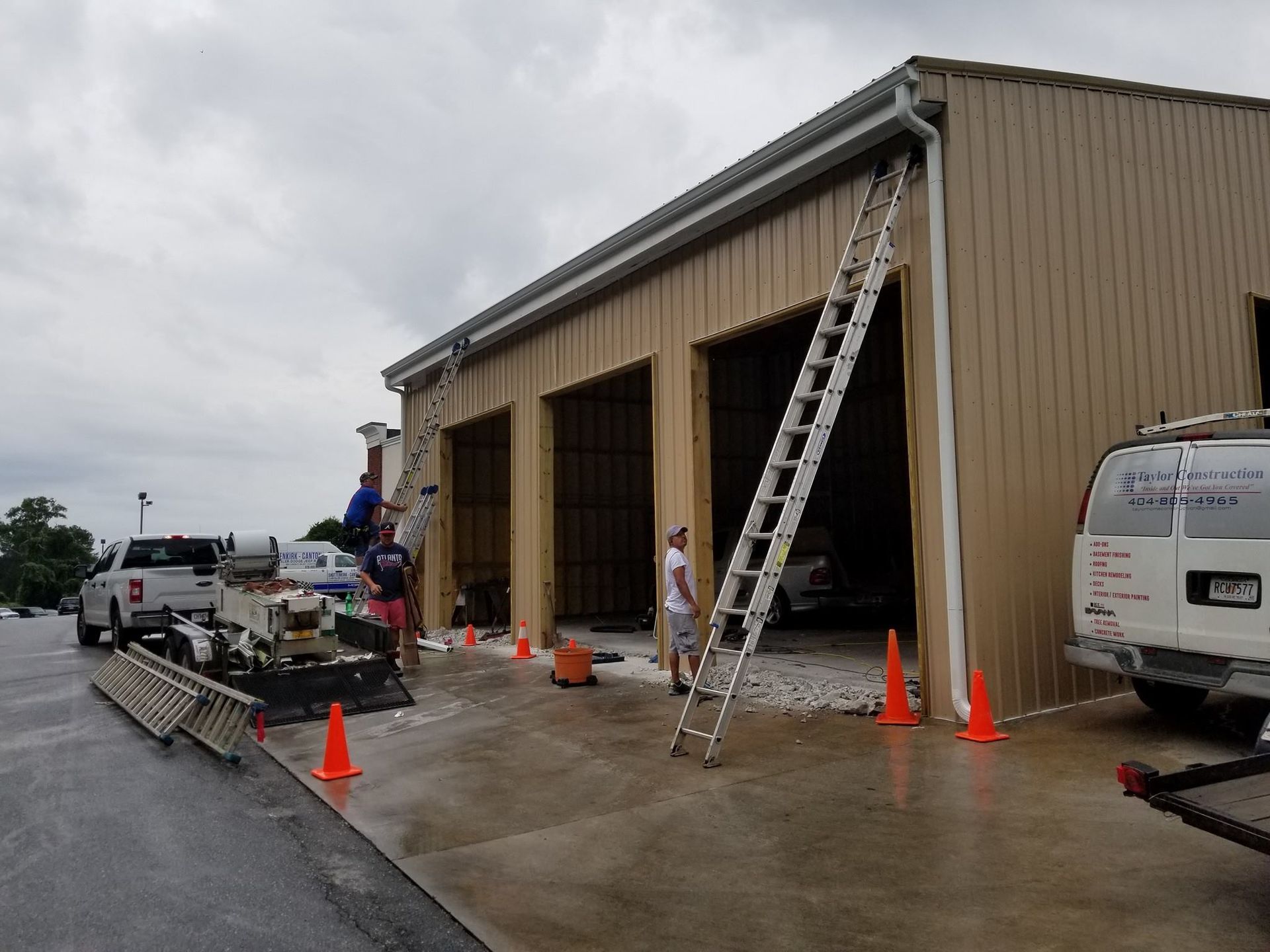 Men installing gutters on a tan building with three garage doors, using ladders.