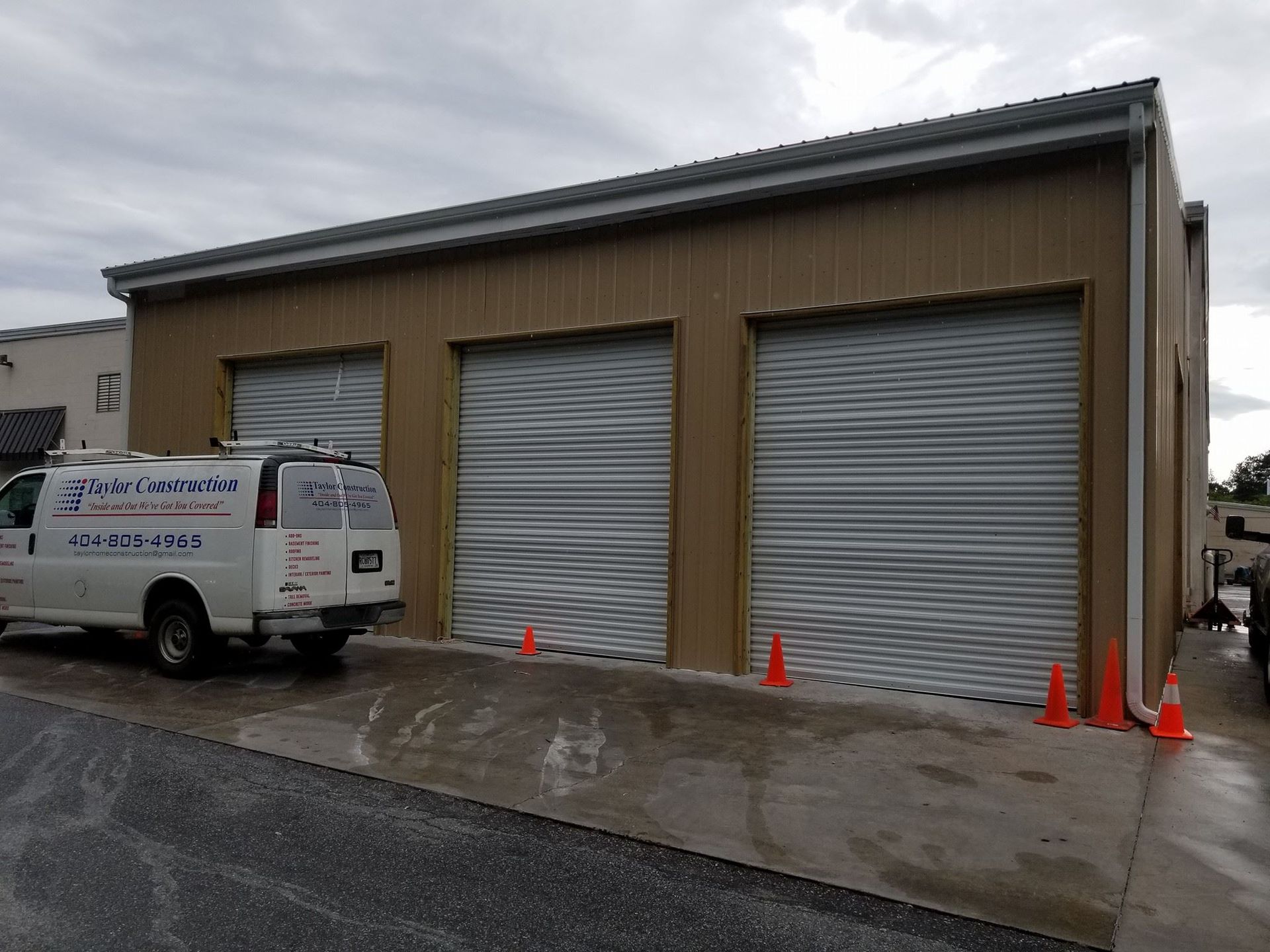 Tan commercial building with three closed garage doors, ramp, and a van parked outside.