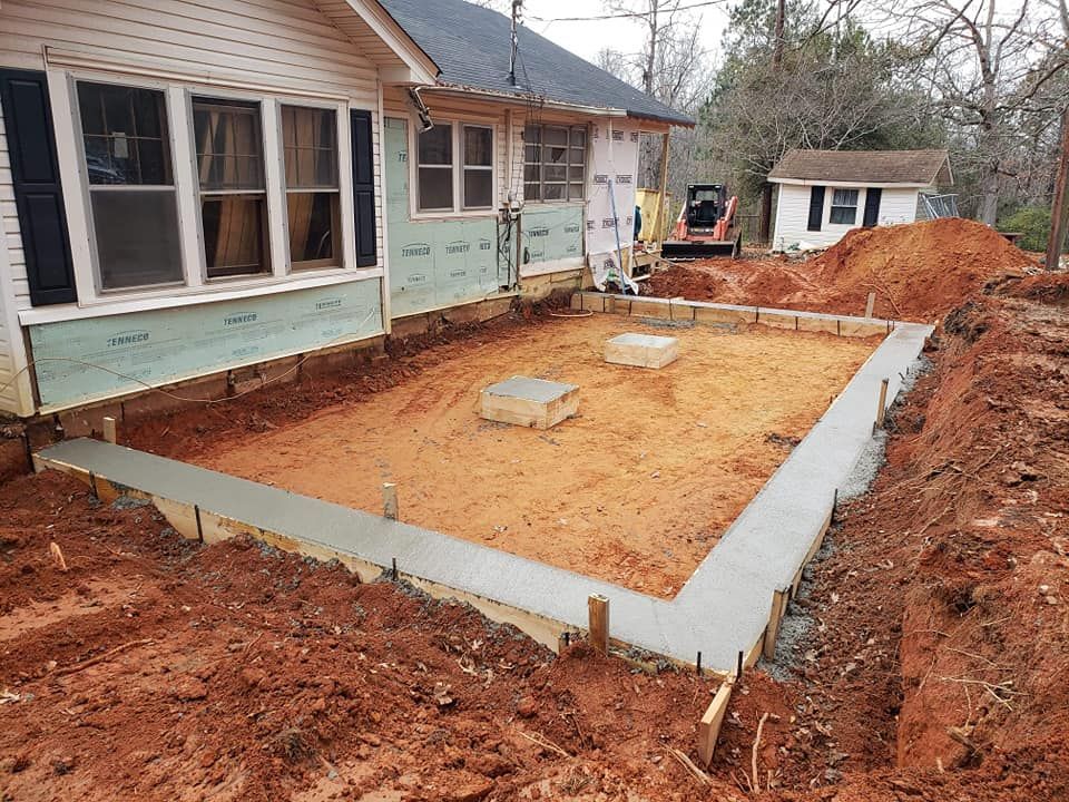 Concrete foundation being built next to a house, surrounded by dirt and construction materials.
