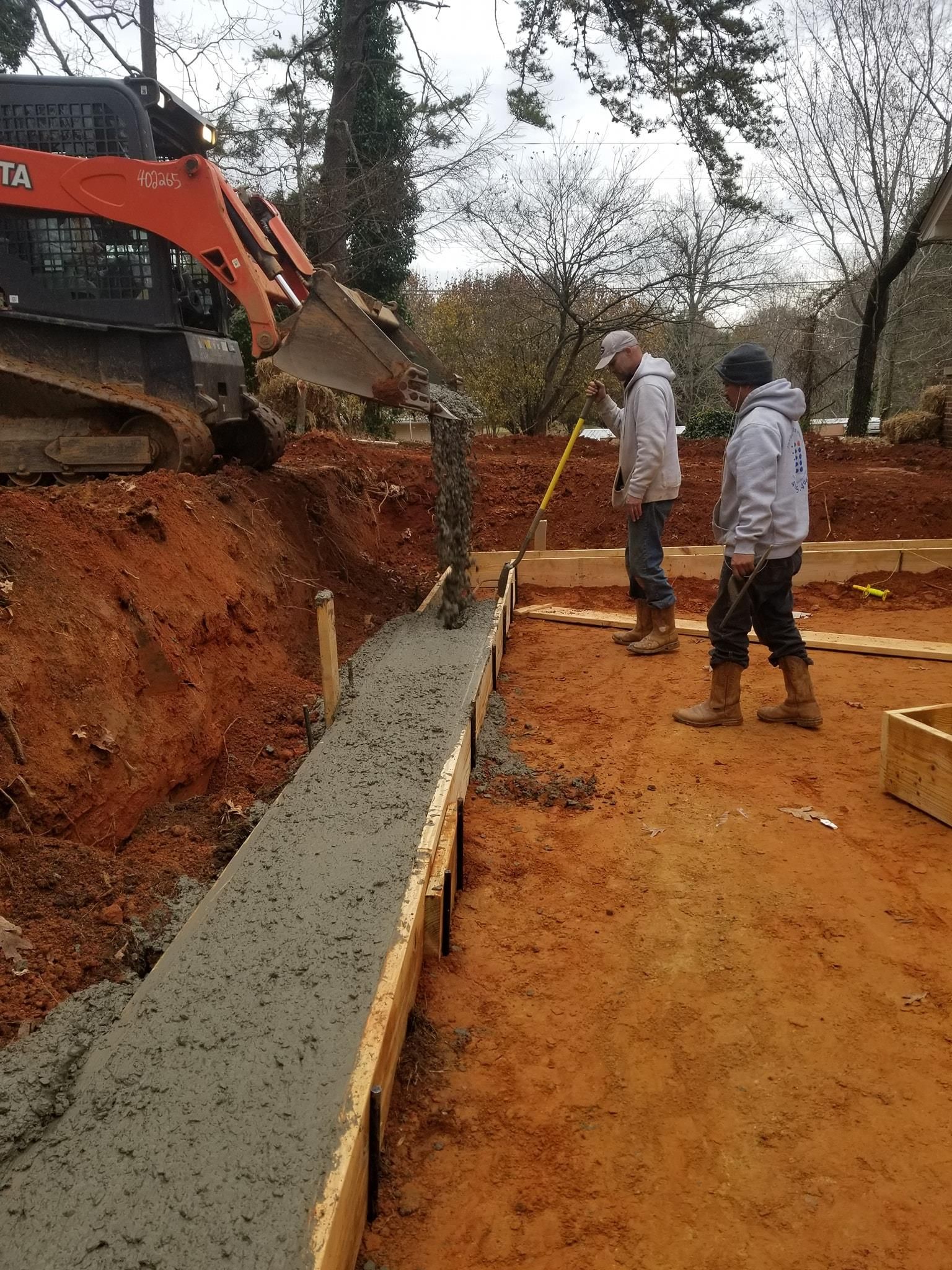 Workers pour concrete with excavator into forms.