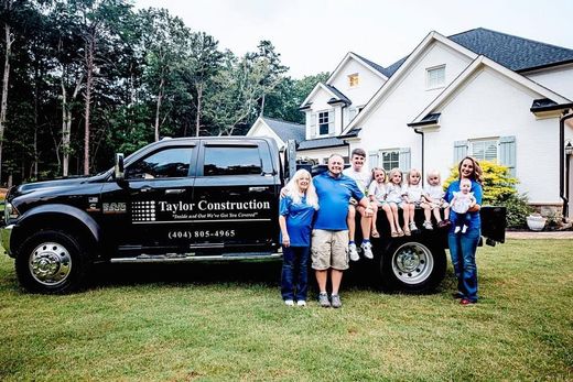 Family with multiple children posing with a black truck in front of a house.
