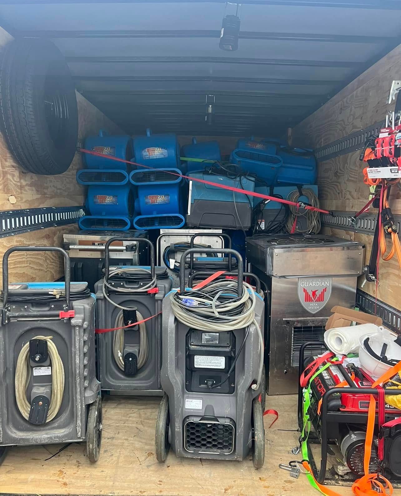 A cargo trailer interior filled with blue air movers, industrial machines, and a generator.