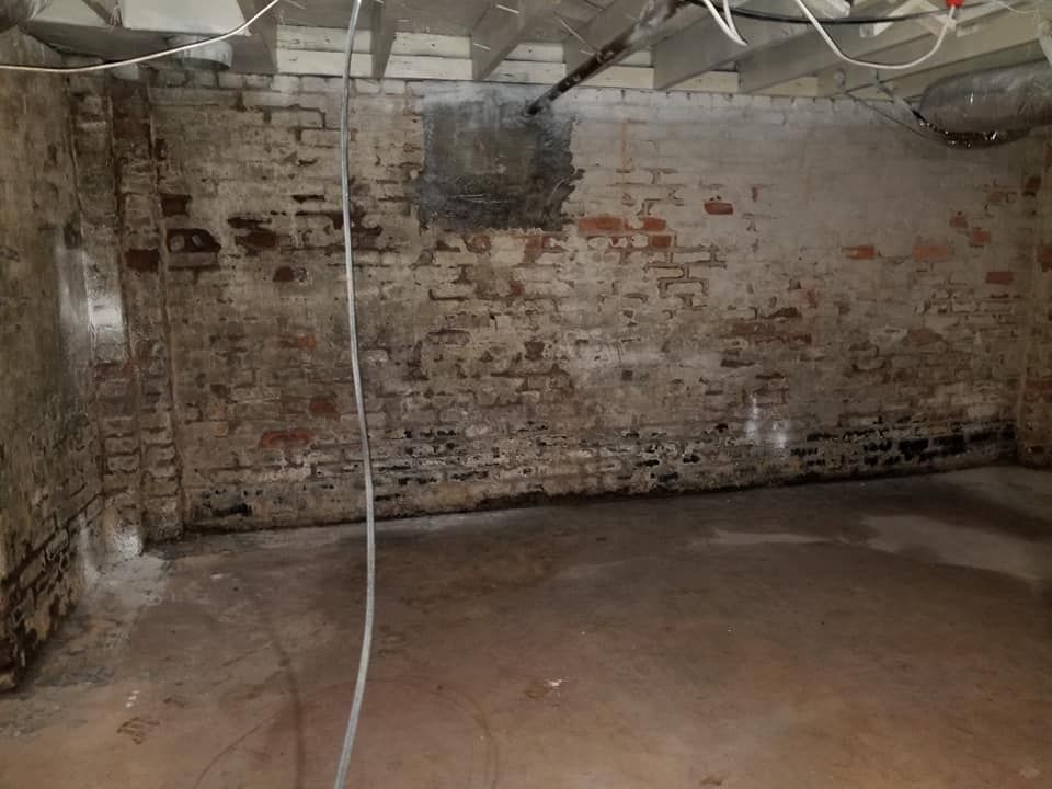 Basement interior with brick walls, concrete floor, and exposed wires.