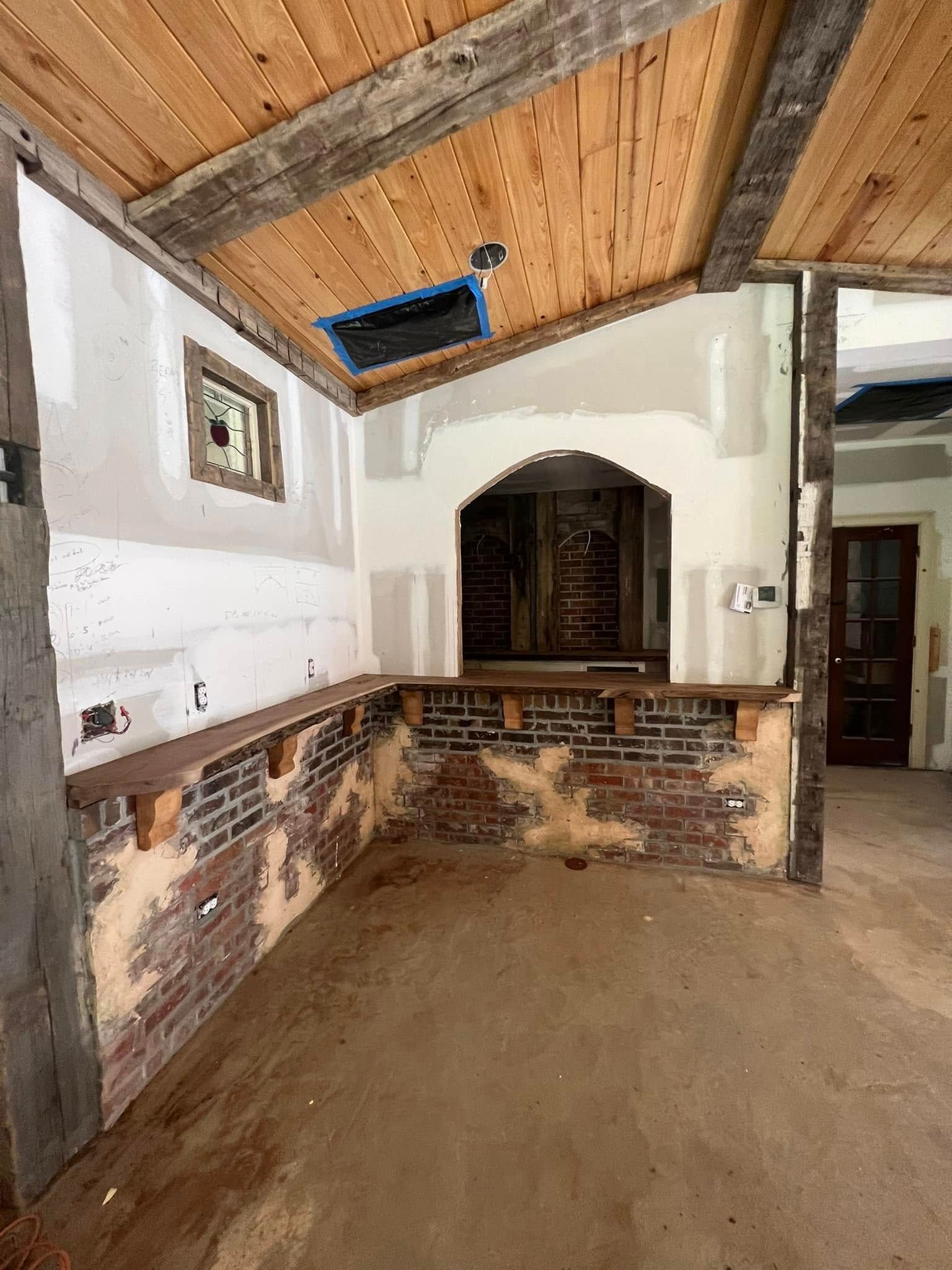 Interior renovation with exposed brick, wood beams, and unfinished walls.