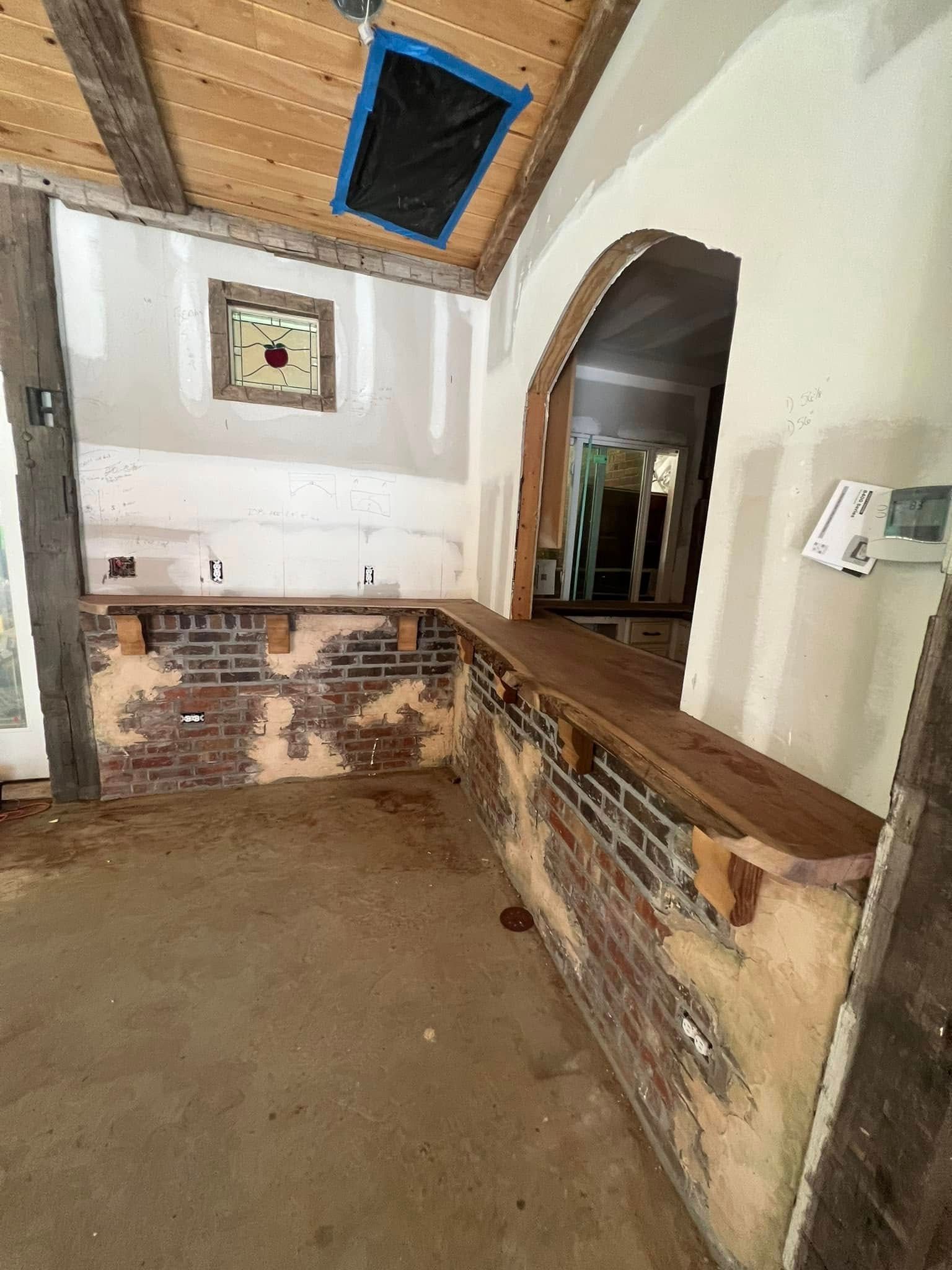 Interior with exposed brick, wood beams, and an arched doorway, under construction.