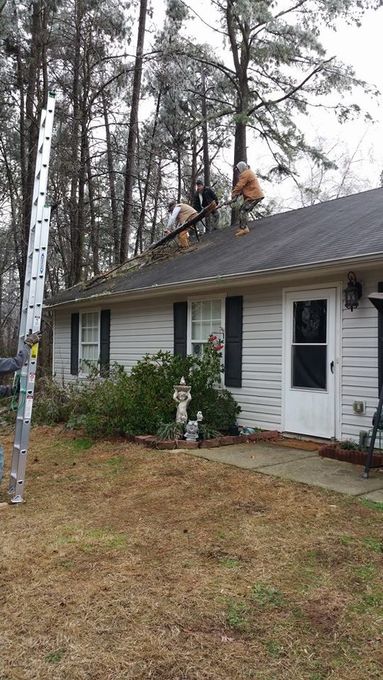 People on a roof cleaning debris. Tall ladder beside the house. Overcast day.