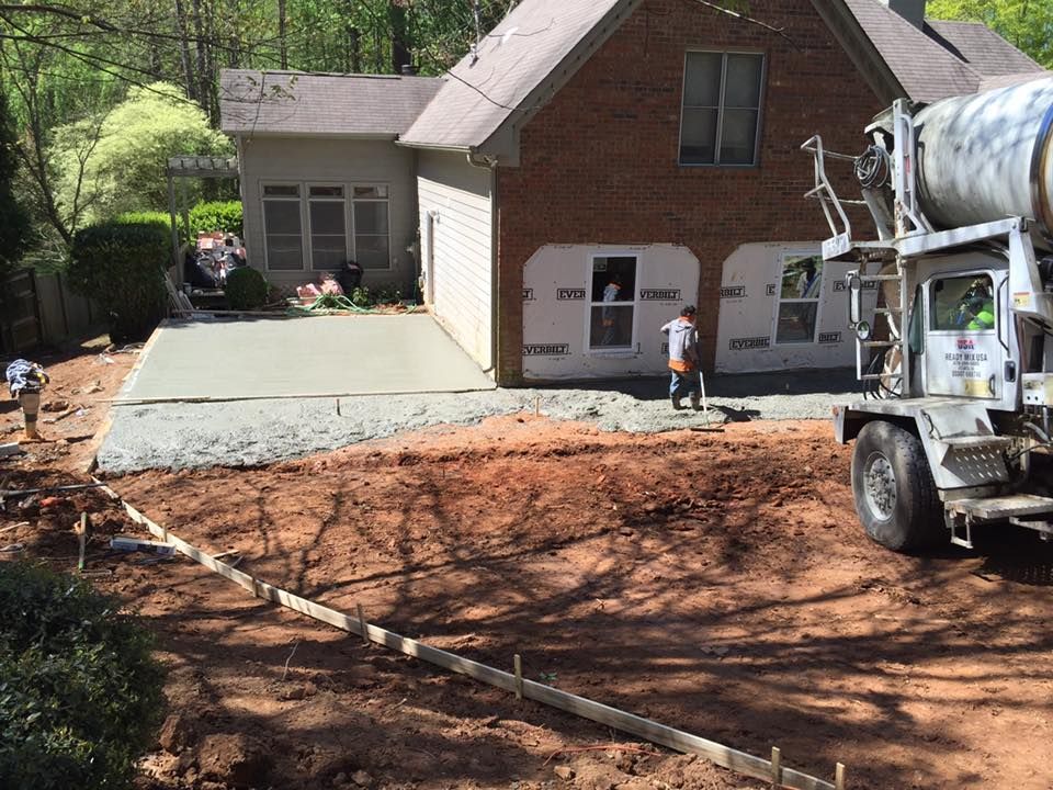 Concrete being poured for patio next to a brick house; workers are present, truck.