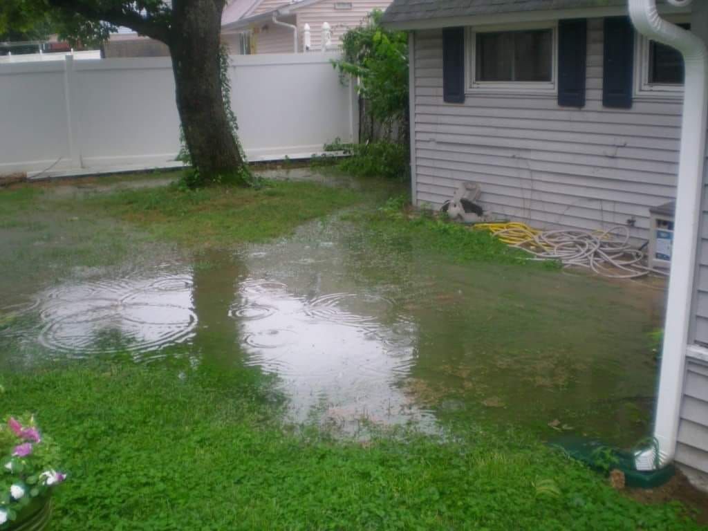 Flooded backyard with standing water, a tree, white fence, and a small building.