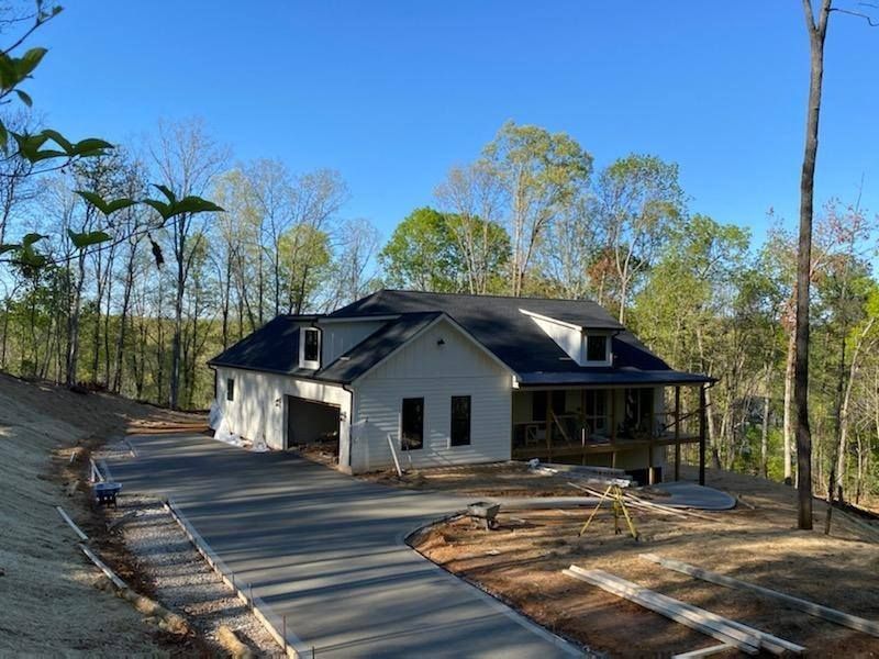 A new two-story house with a driveway and garage is being built in a wooded area under a clear blue sky.
