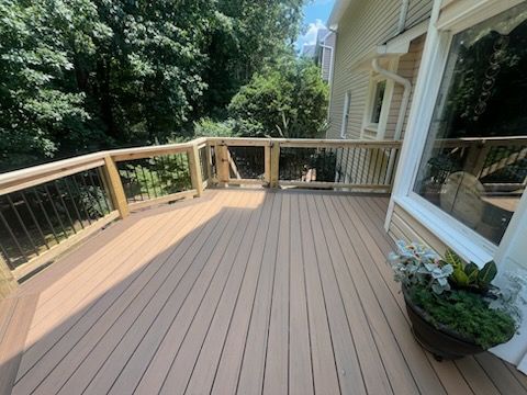Wooden deck with brown planks, railing, and view of trees and house.