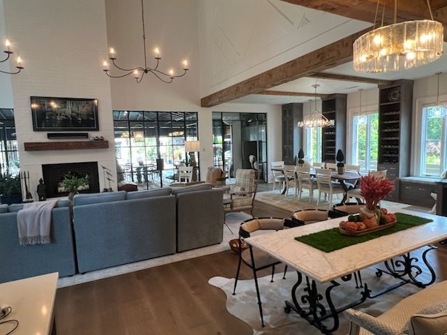 Spacious living area with fireplace, dining table, and open-concept kitchen with wood beams, windows, and a rug.