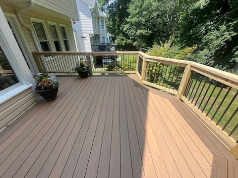 A wooden deck with railings and potted plants; a house and trees are in the background.