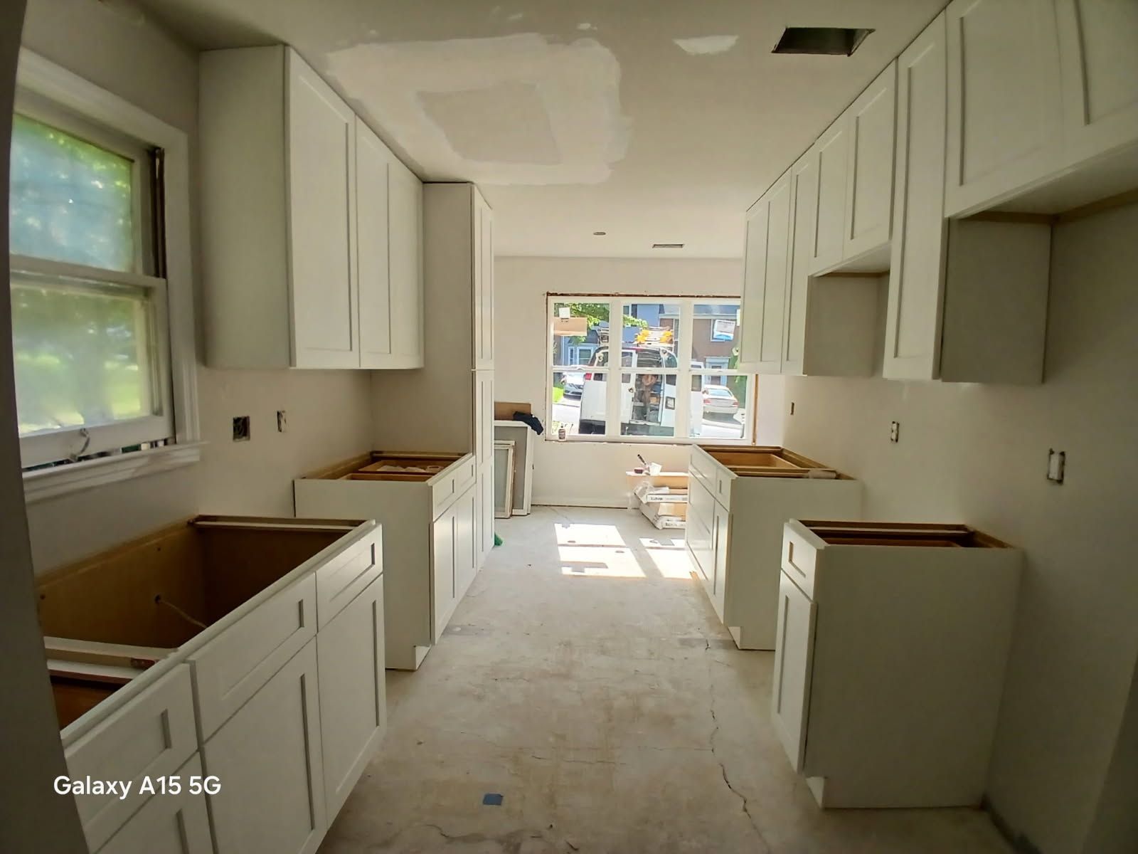 Kitchen renovation: white cabinets installed along walls, unfinished countertops, window at far end.