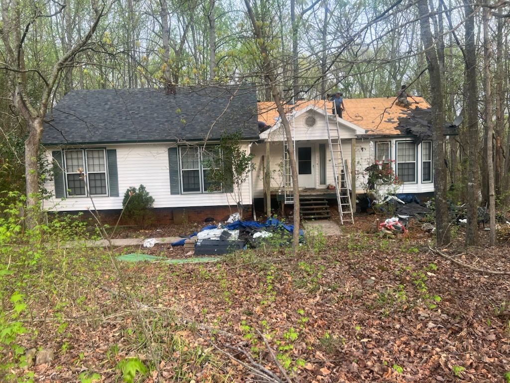A house with a new roof being installed; the yard has debris and overgrown foliage.