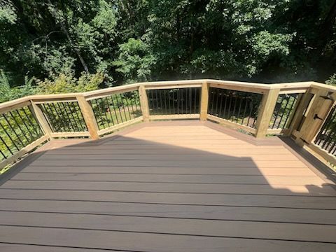 Wooden deck with brown composite flooring, surrounded by a railing with black spindles, set against a backdrop of trees.