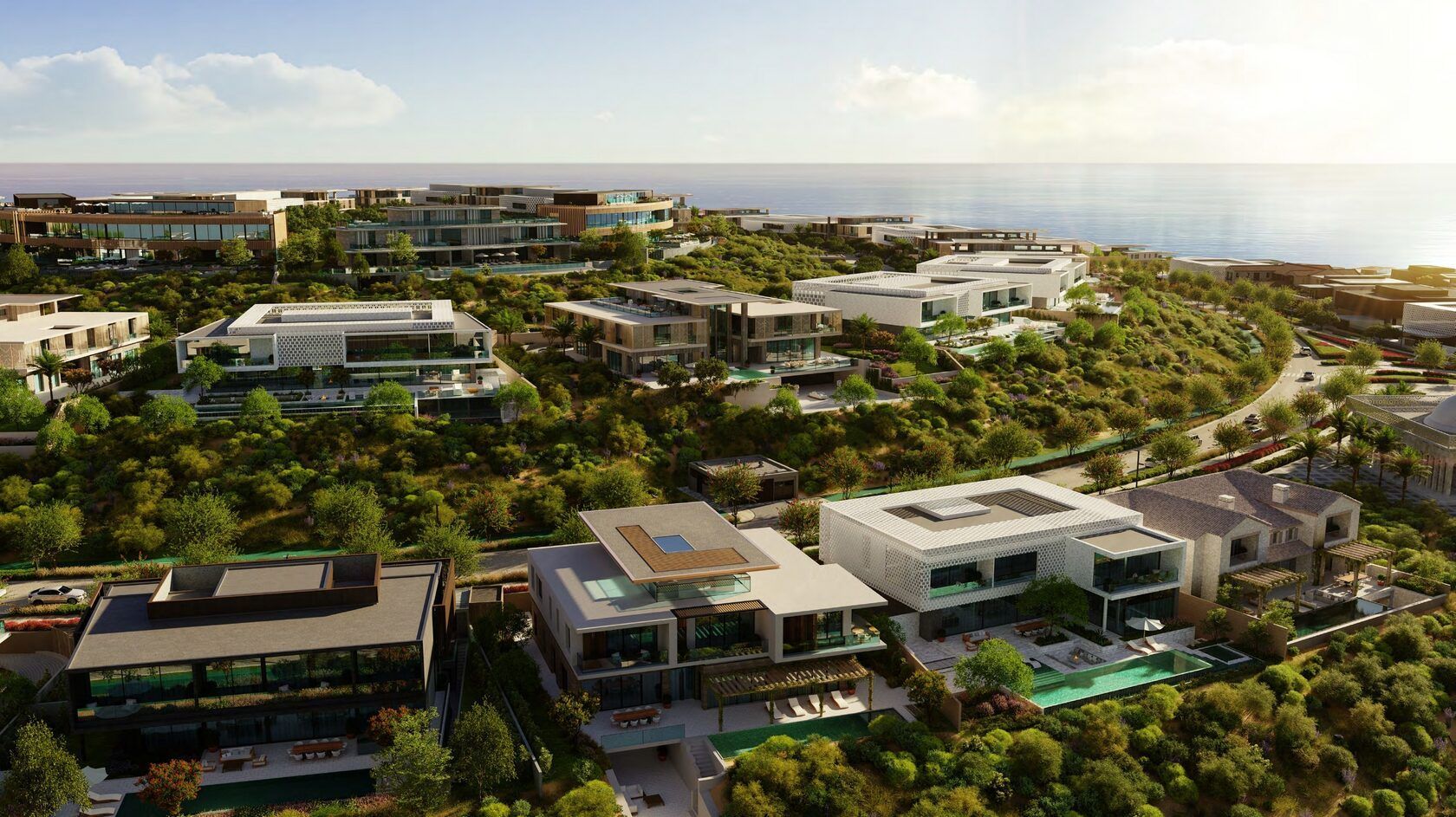 Aerial view of luxury homes on a hillside overlooking the ocean; lush greenery, modern architecture, sunny day.