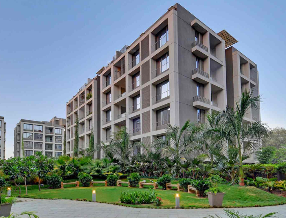 Modern gray apartment buildings with boxy balconies, green landscaping, and palm trees.
