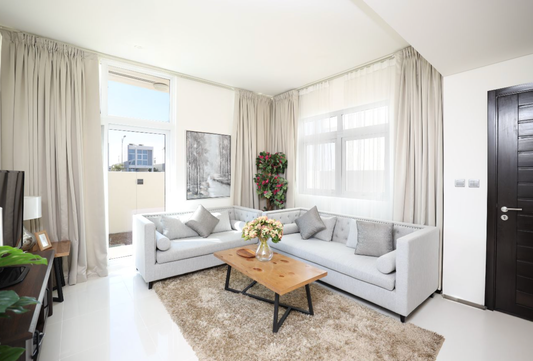 Bright living room with gray sectional sofa, light curtains, wooden coffee table, and area rug.
