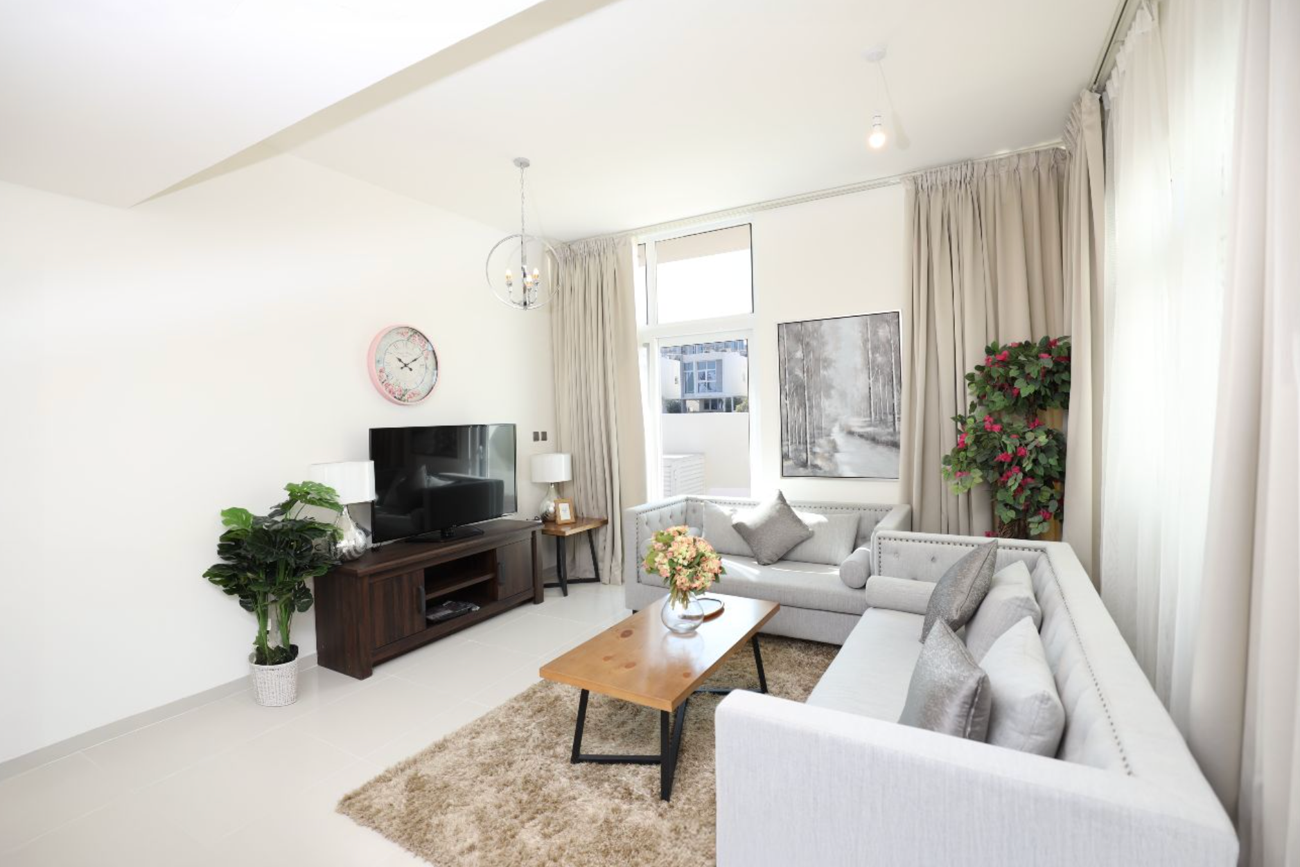 Living room with a white sofa, dark TV stand, and neutral-toned rug, with a large window and drapes.