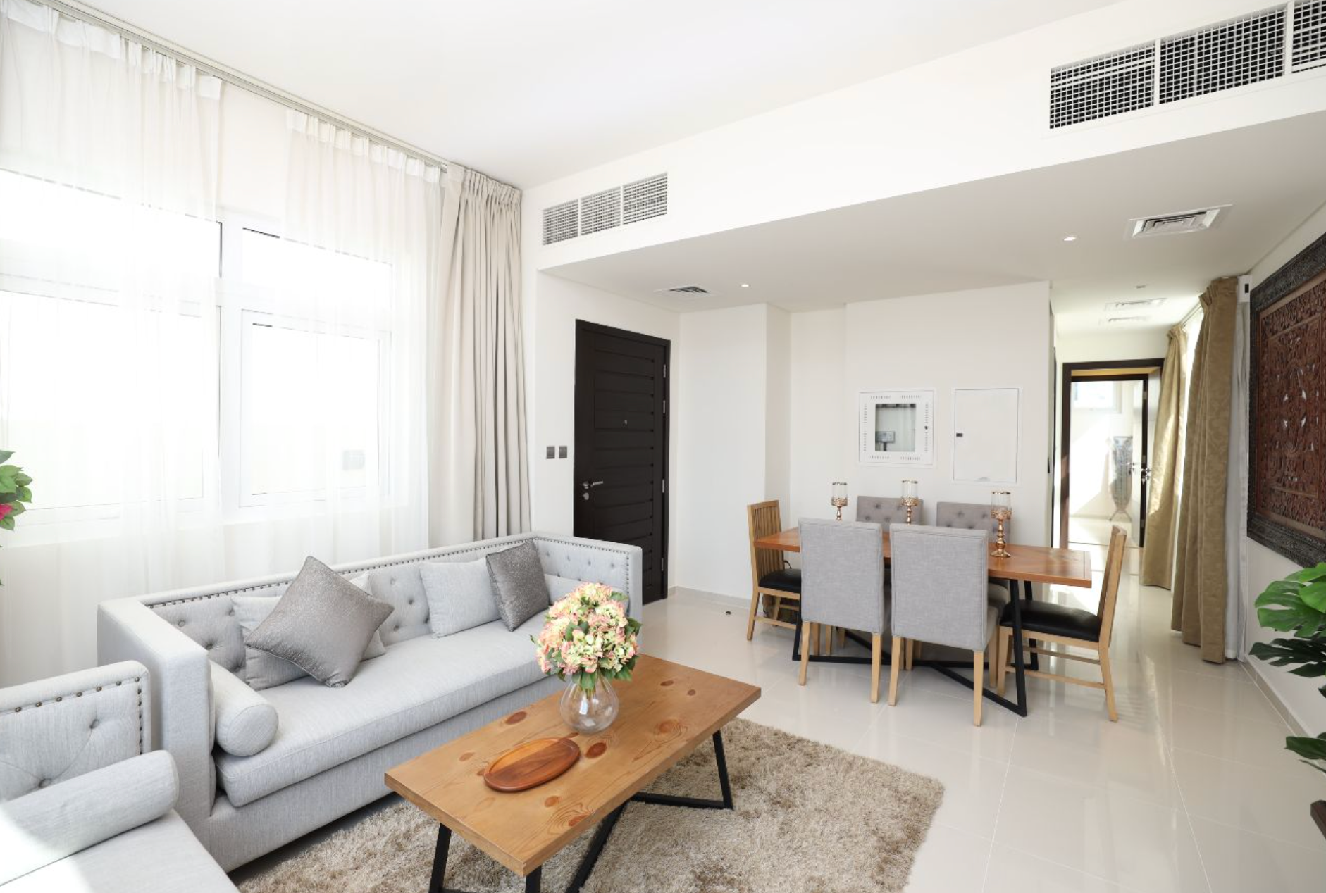 Bright living room with gray sofa, wooden table, and dining set.