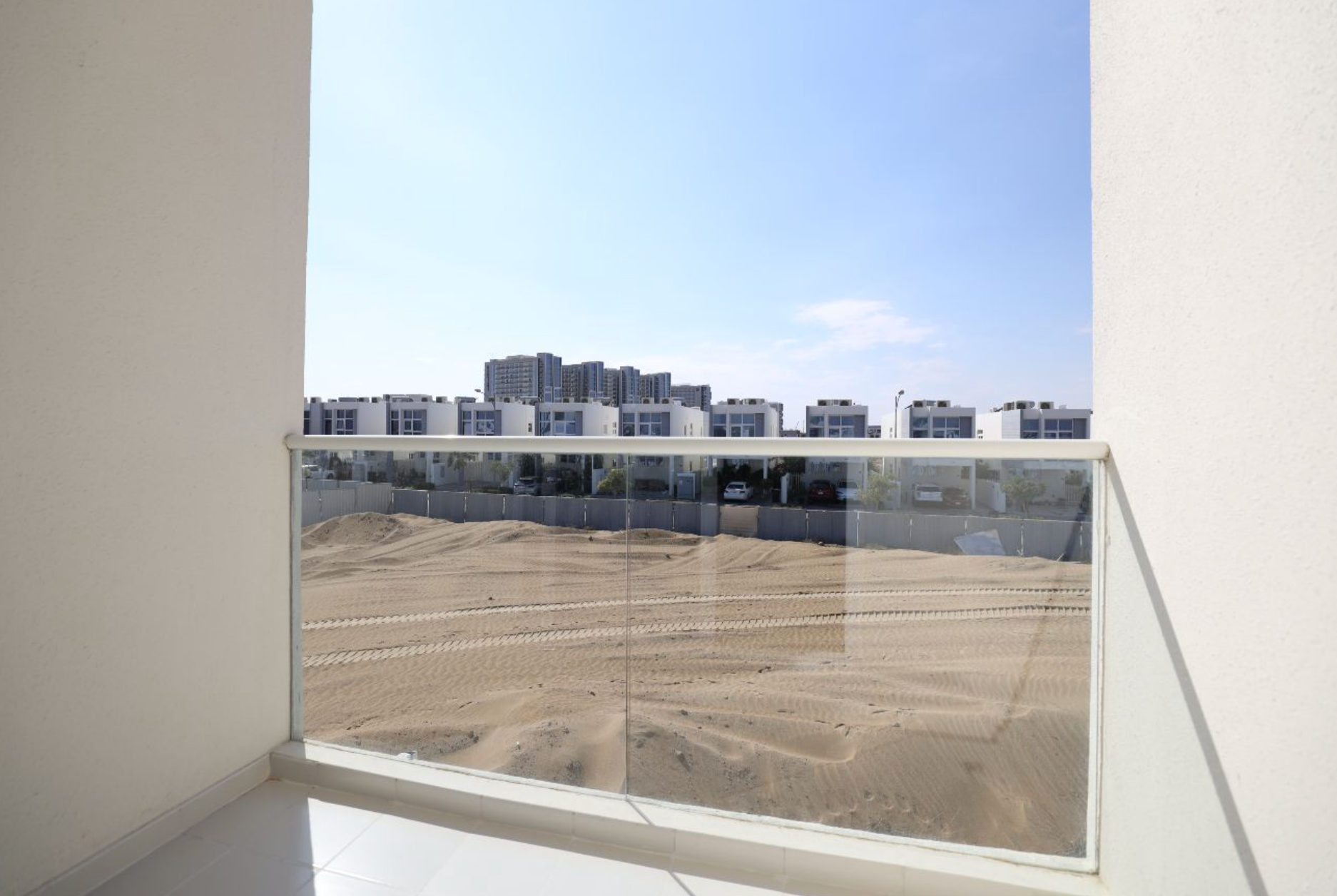 View from a balcony with a glass railing, looking out at a construction site and buildings under a blue sky.