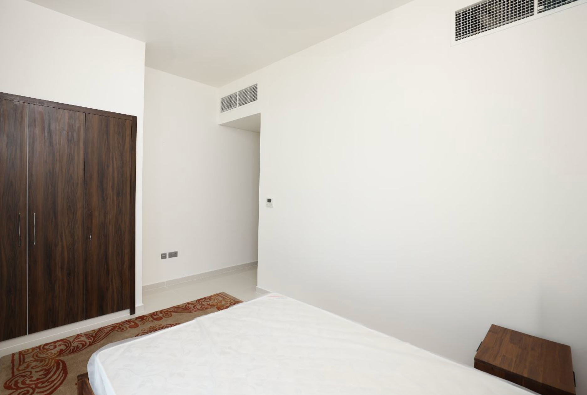 Bedroom interior with a white bed, wooden closet, and white walls.
